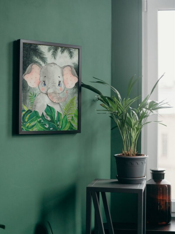 Framed watercolor illustration of a baby elephant surrounded by jungle foliage, hanging on a deep green wall above a small table holding a potted palm.